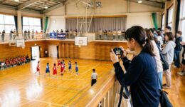 体育館の2階席からミニバスの試合を撮影する保護者
